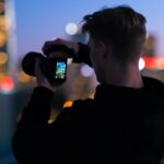 man in black jacket taking photo of city lights during night time